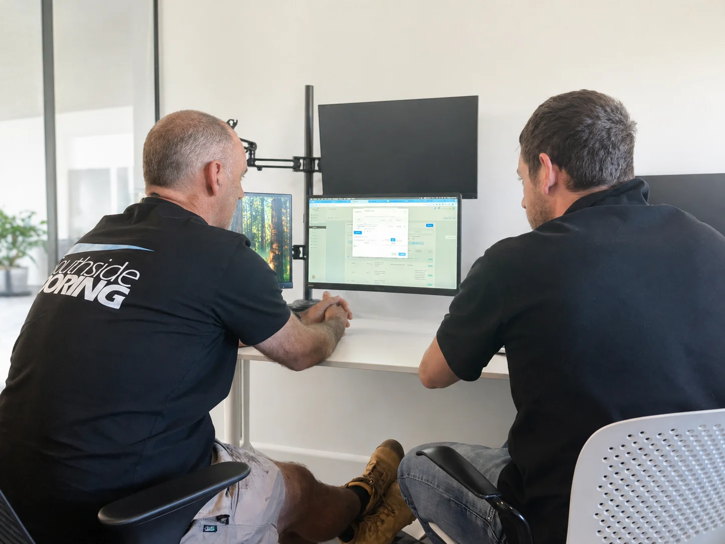 Send a Tradie team reviewing job management software on dual monitors in a modern office